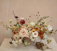 a vase filled with lots of different flowers on top of a white table next to a wall