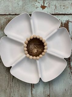 a white flower shaped plate with beads in the center on an old wooden table top