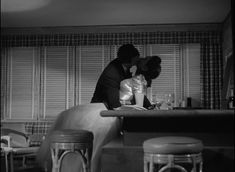 black and white photograph of two people at a table in a restaurant, one kissing the other's head