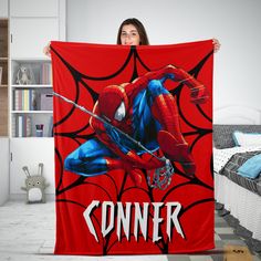 a woman holding up a red blanket with the image of spider - man on it