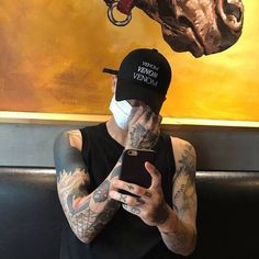 a tattooed man wearing a mask and holding a cell phone