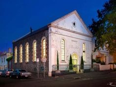 an old church is lit up at night with cars parked in the parking lot behind it