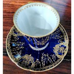 a blue and gold tea cup sitting on top of a wooden table next to a saucer