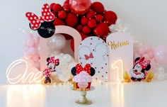 a table topped with lots of balloons and minnie mouse figurines next to a sign