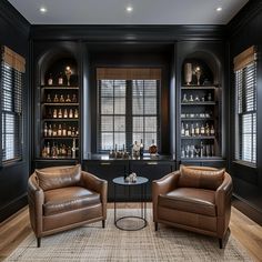 two brown leather chairs sitting next to each other in a room with black walls and wooden floors