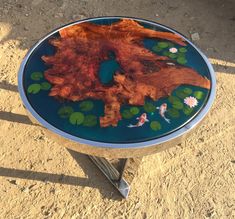 a glass table with flowers and leaves painted on the top is sitting in the dirt