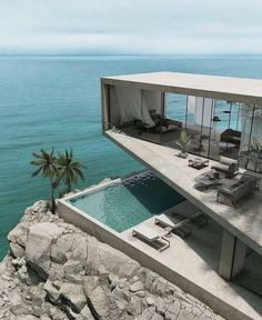 an aerial view of a house overlooking the ocean with lounge chairs and palm trees on the cliff