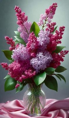 a glass vase filled with purple flowers on top of a pink cloth covered tablecloth