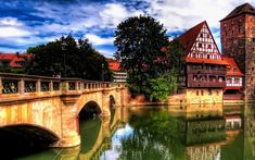 a bridge that is over some water with buildings in the background and trees on both sides