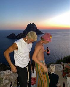 a man and woman standing next to each other on top of a hill near the ocean