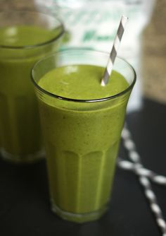 two glasses filled with green smoothie sitting on top of a table