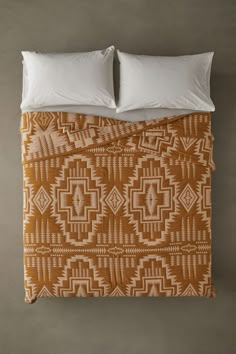 an orange and white comforter with two pillows on top of it, in front of a gray wall