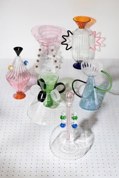 several different colored glass vases sitting on a white tablecloth with polka dot dots