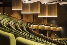 an auditorium with rows of green seats and wooden paneling on the walls, along with lights hanging from the ceiling