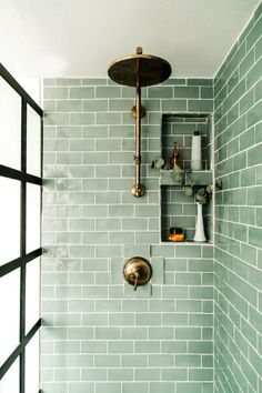 a green tiled shower with brass fixtures and shelves on the wall, along with vases