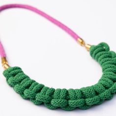 a crocheted necklace with pink cord and gold clasp on white background, closeup