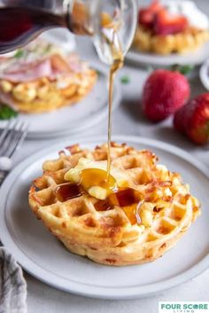 waffles with syrup being drizzled over them on plates next to strawberries