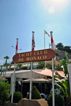 a sign that says yacht club de monaco in front of some flags and bushes on the sidewalk