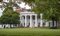 a large white house with columns and pillars on the front, surrounded by lush green trees