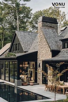 A rustic modern home with a stone chimney and large glass windows, opening to a serene poolside area surrounded by lush greenery, offering a perfect blend of natural warmth and contemporary design. Stone Chimney, House Landscaping