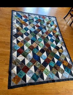 a multicolored quilt on the floor in front of a chair and wooden floor