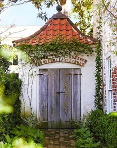 an old door is surrounded by greenery and brick walls in front of a white house