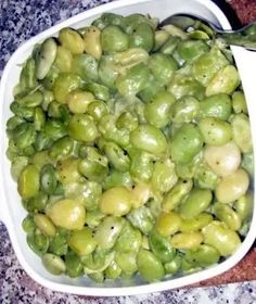 a white bowl filled with green olives on top of a counter next to a spoon