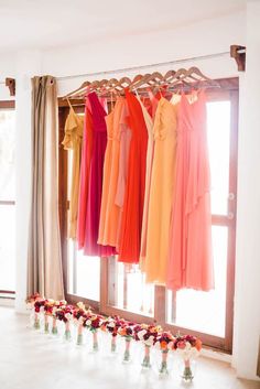 the bridesmaids'dresses are hanging in front of an open window, with vases filled with flowers