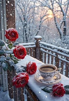 a cup of coffee sitting on top of a table covered in snow next to red roses