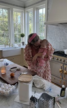 a woman holding a baby while standing in a kitchen