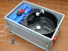 an open plastic container on the ground with various items in it and wires attached to the lid