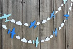 blue and white paper airplanes are hanging from a string on a wooden fence with clouds