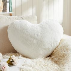 a white heart shaped pillow sitting on top of a bed next to pillows and flowers