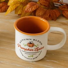 a cup of coffee sitting on top of a wooden table next to leaves and pumpkins