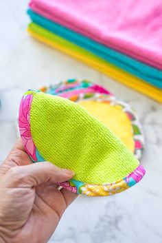 a person is holding up a small green and pink hat on top of a table