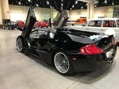 a black sports car with its doors open in a showroom filled with other cars