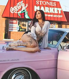 a woman sitting on the hood of a pink car