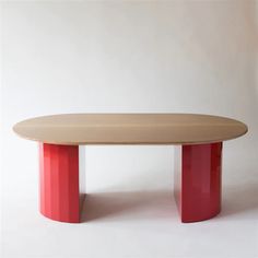 an oval table with red legs and a wooden top on a white background in front of a plain wall