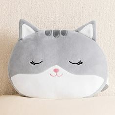 a gray and white cat shaped pillow sitting on top of a bed next to a wall