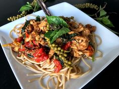 a white plate topped with pasta and meat covered in sauce, garnished with green leaves