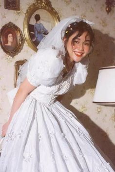 a woman in a white wedding dress posing for a photo next to a wall with pictures on it