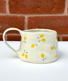 a white ceramic pitcher with lemons painted on it's sides, sitting against a brick wall