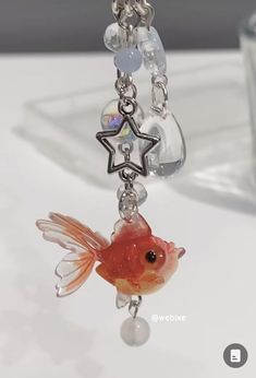 a goldfish is hanging from a chain on a white surface with a glass cup in the background