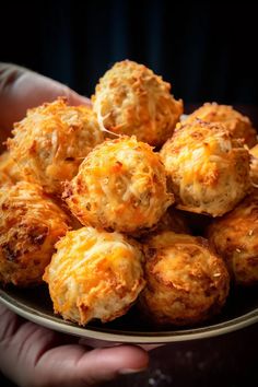 a person holding a plate full of cheesy cheese ball bites in their hands