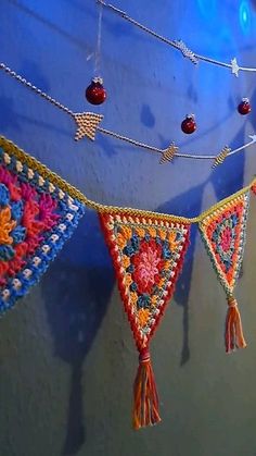 colorful crocheted decorations hanging from a blue wall with beads and tassels