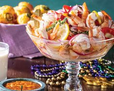 a glass bowl filled with shrimp and vegetables next to a cup of orange juice on a table