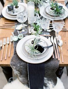 the table is set with silverware, plates and succulents on it