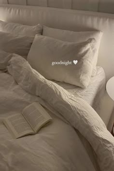 an open book sitting on top of a bed next to two pillows and a night stand