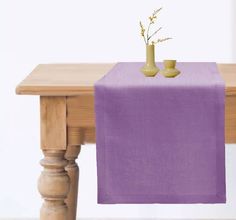 a table topped with a vase filled with flowers next to a purple cloth covered table