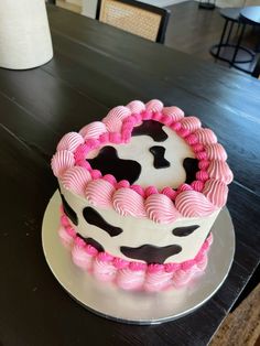 a cake decorated with pink and black icing on top of a wooden table next to a white vase